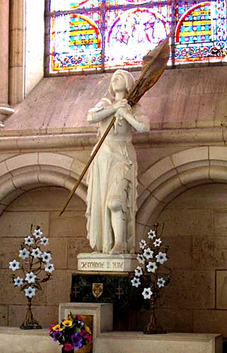 Picture of a statue of Joan of Arc holding her flag across her chest inside a church in France